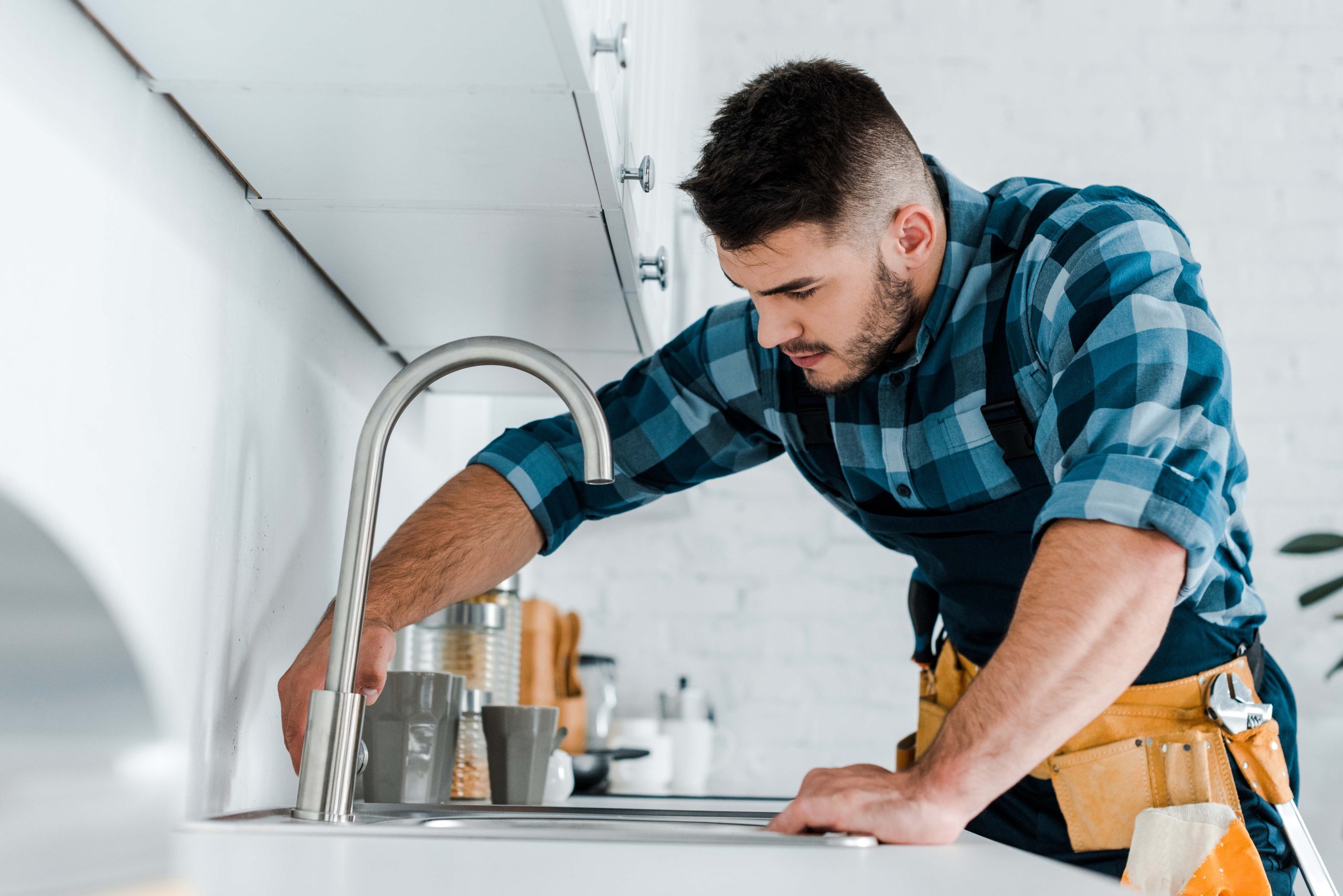 selective focus of handsome handyman working near sink in kitche