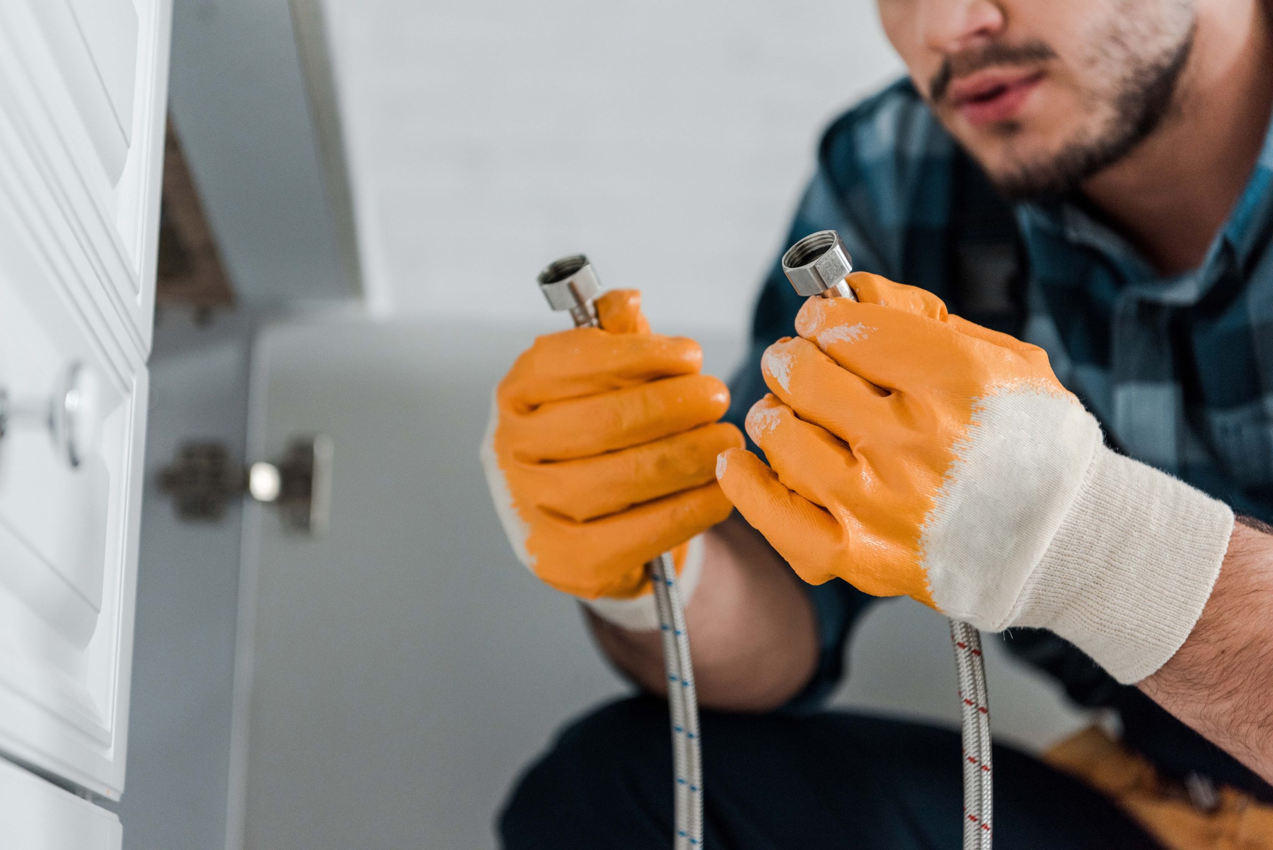 selective focus of handyman holding metal hose near kitchen cabi