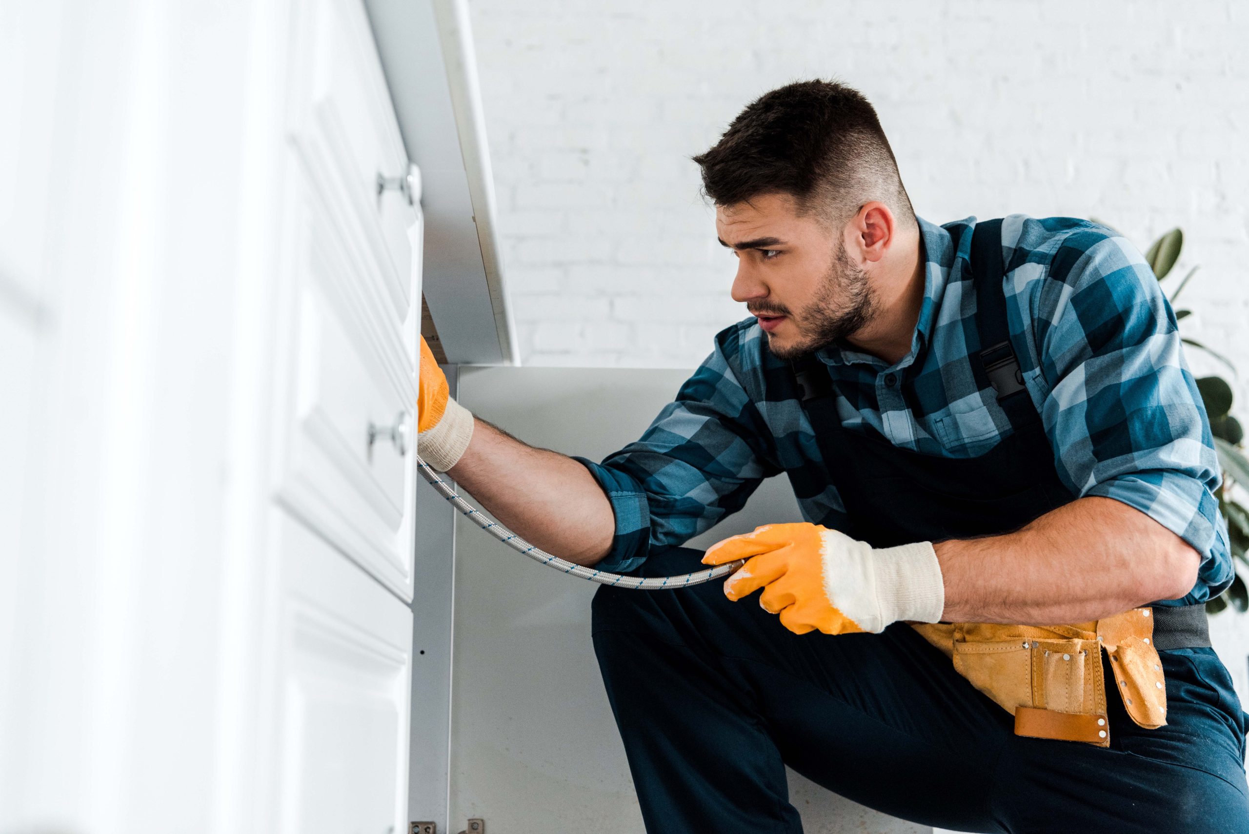 selective focus of repairman holding metal hose near kitchen cab