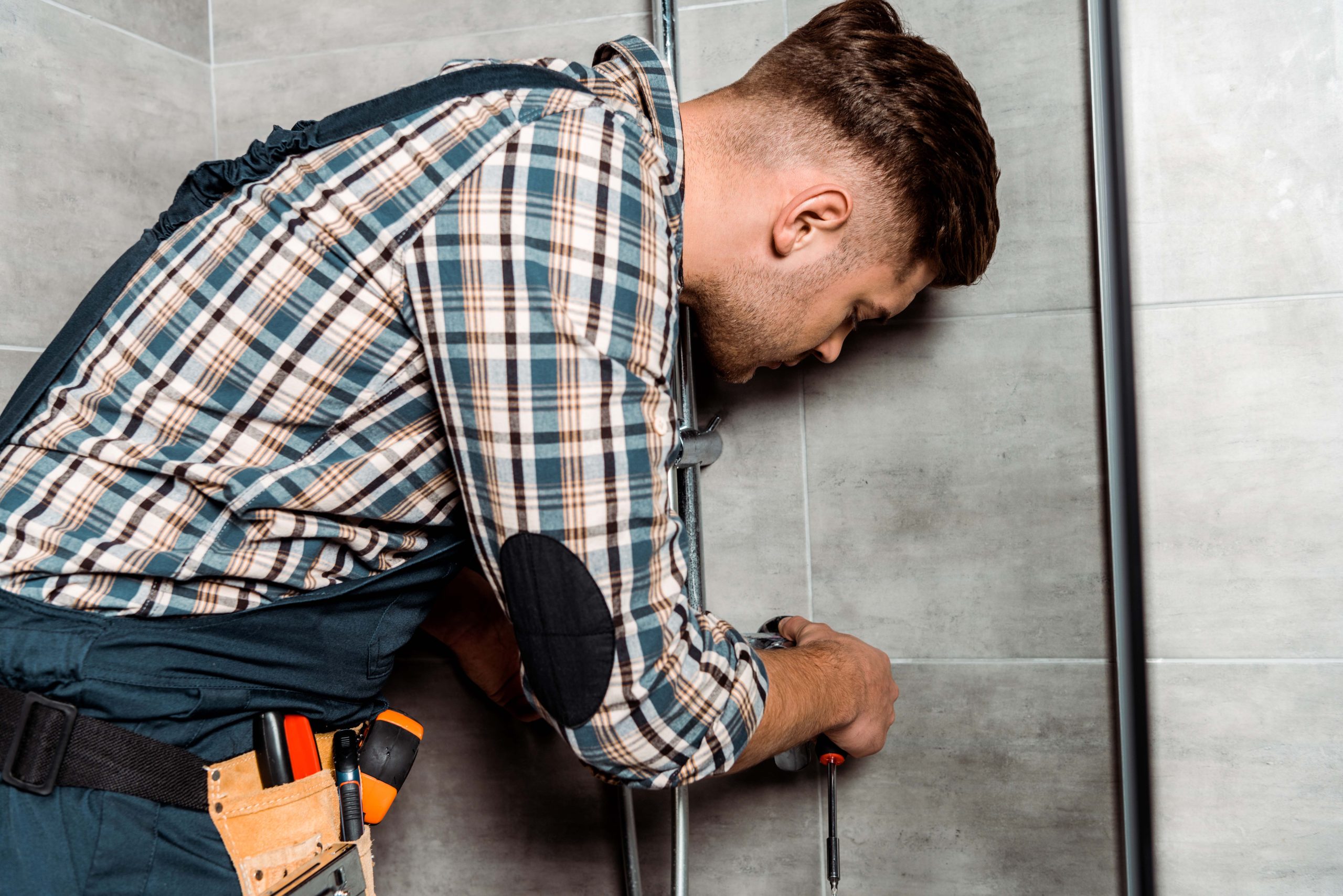 serious installer in overalls standing in bathroom near pipe