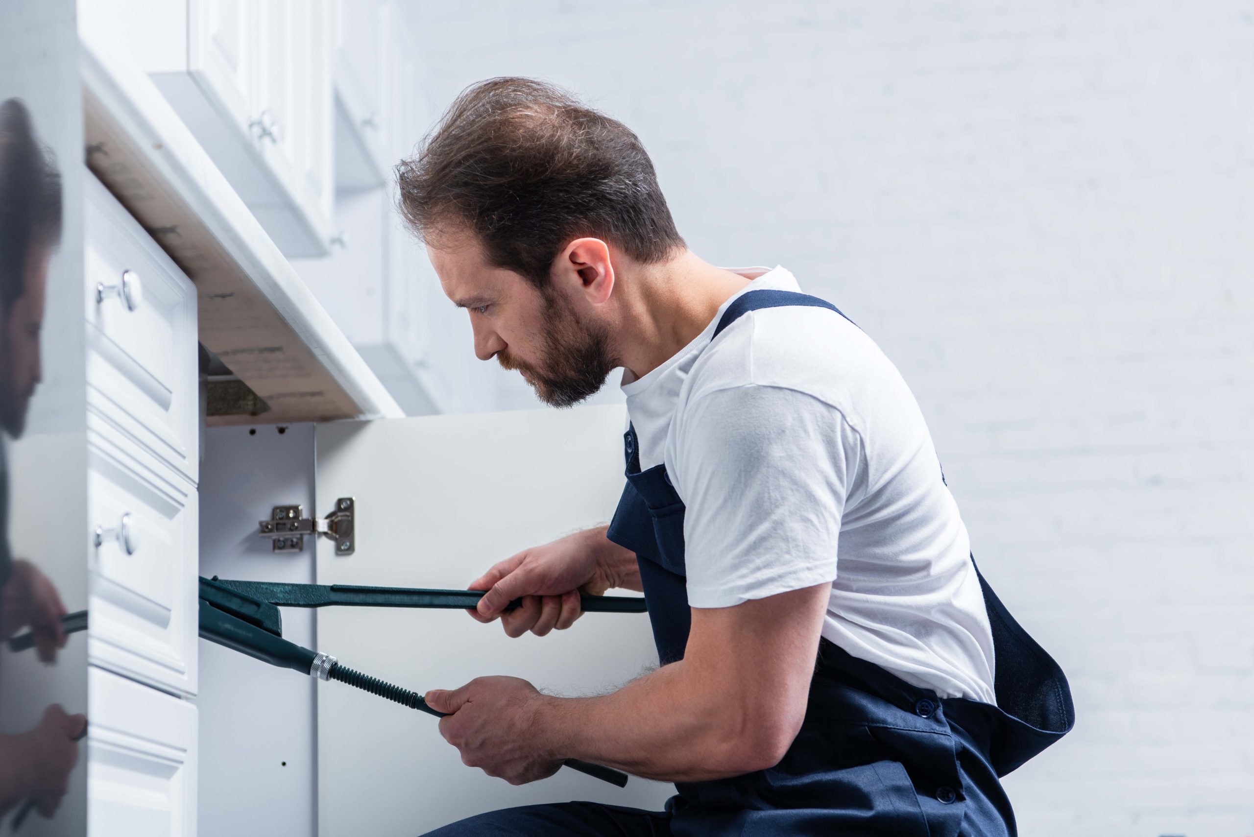 side view of adult bearded repairman in working overall fixing s