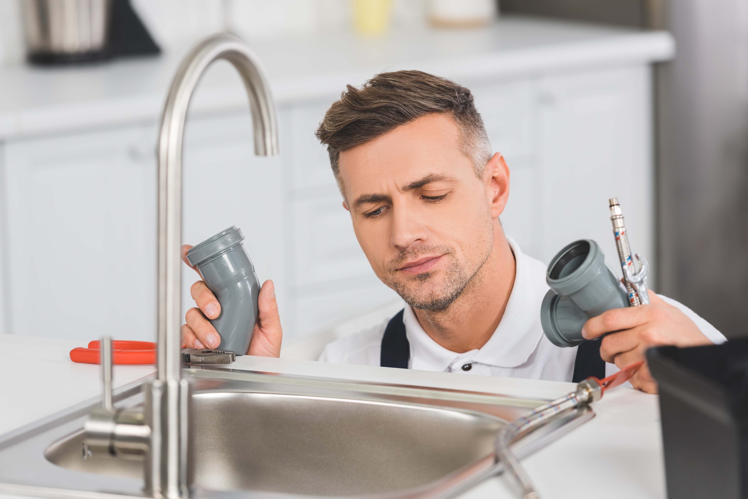 thoughtful adult repairman holding pipes and tools while repairi