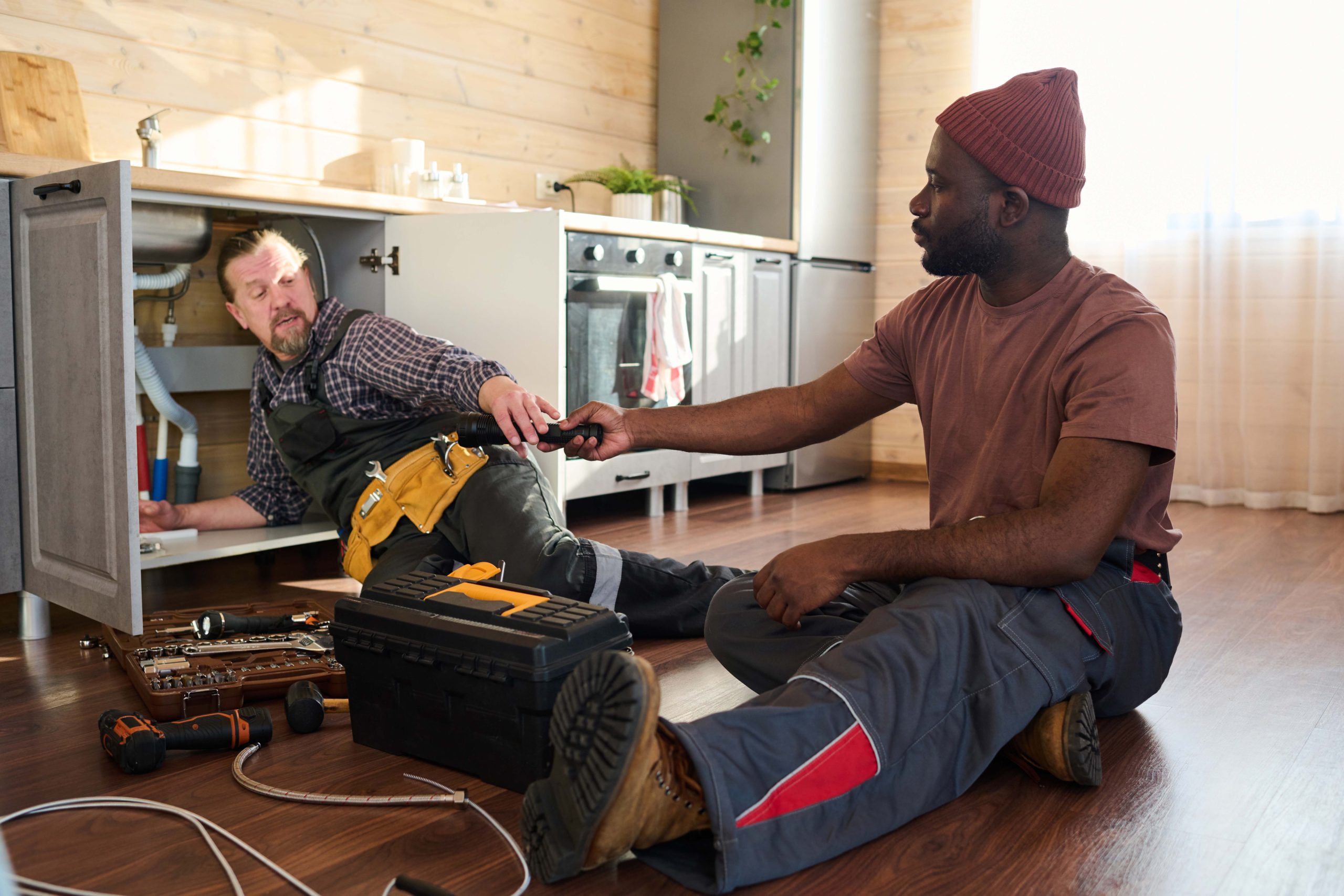 young black man in workwear passing handtool to mature colleague