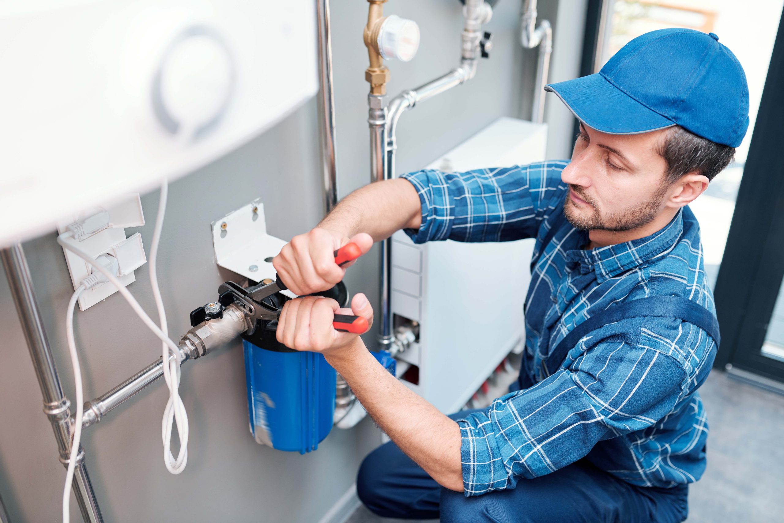 young man in workwear using pliers while installing water filtration system